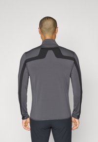 Long-sleeve athletic top in charcoal gray with black accents, featuring a high collar and stretch fabric for flexibility, smooth texture, and fitted design.