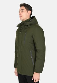 Giacca verde khaki con cappuccio, zip frontale e due tasche con zip. Tessuto liscio e silhouette aderente, con colletto alto.
