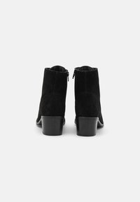 Botas de tornozelo em camurça preta com bico arredondado, salto bloco baixo e fecho de correr na parte de trás. Textura suave com um design simples e limpo.