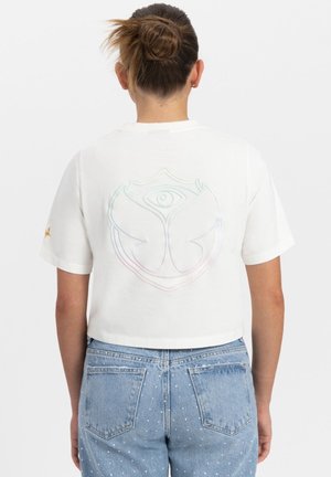 Witte cropped t-shirt met een kleurrijk, reliëf logo op de achterkant; gecombineerd met lichtblauwe denim shorts versierd met kleine witte stippen.
