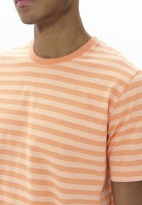 Short-sleeve t-shirt made of soft fabric, featuring horizontal stripes in light orange and white, with a crew neckline and stitched edges.