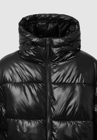 Giubbotto imbottito nero con una finitura lucida e trapuntata, colletto alto e chiusura frontale con zip. Presenta cuciture arricciate e un cordoncino elastico sul cappuccio.