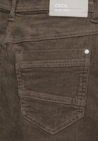 Hnědá kordová látka s vertikálními žebry, obsahující jednu zadní kapsu a detail kovového nýtu. Na štítku je nápis "CECIL WE LOVE SKIRTS."