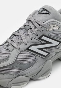 Primer plano de una zapatilla New Balance 9060 gris con paneles de malla, suela gruesa texturizada y cordones cruzados.