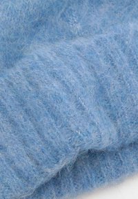 Țesătură tricotată de culoare albastru deschis, cu o textură moale și pufoasă, având modele subtile de nervuri. Materialul pare cald și confortabil.