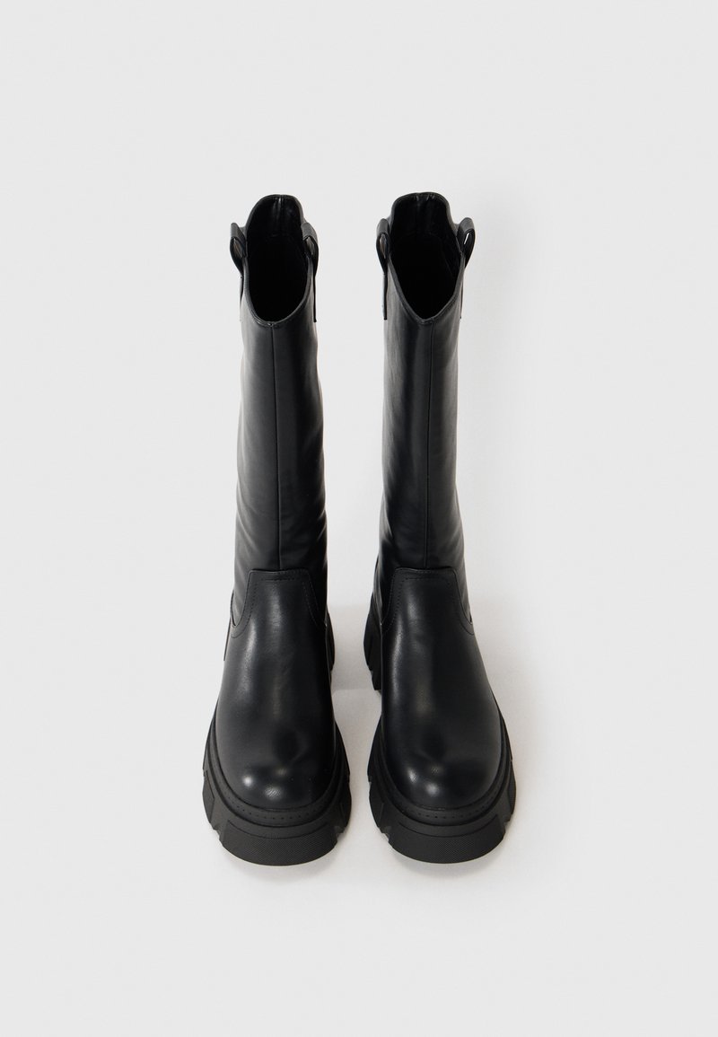 Een paar hoge zwarte leren laarzen met stevige zolen, rechtopstaand op een plain witte achtergrond.