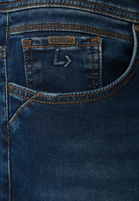 Ciemnoniebieskie dżinsy z tylną kieszenią z pomarańczowym przeszyciem i srebrną metką z napisem "LANCERTO". Są widoczne subtelne przetarcia.