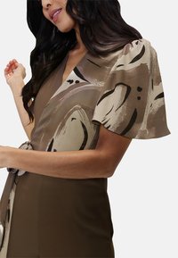 Brown wrap dress featuring short sleeves with a cream and black abstract pattern, textured fabric, and a tie belt at the waist.