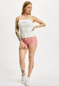 Top din bumbac alb cu dungi, având inscripția "Iubește-mă acum"; pantaloni scurți din denim roșu cu un model decolorat. Model purtând adidași albi, evidențiind tatuaje.