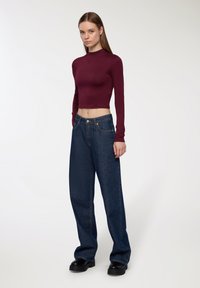 Top crop a maniche lunghe bordeaux abbinato a jeans a gamba larga blu scuro. Footwear chunky neri completa l'outfit. Texture lisce evidenti.