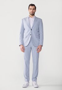 Hellblau gestreifter Anzug mit Reverskragen, Knopfschluss und passender Hose. Ein weißes Hemd und weiße Sneaker runden den Look ab.