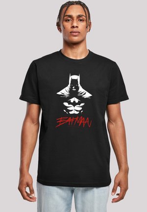 Schwarzes Baumwoll-T-Shirt mit einem weißen Motiv eines Superhelden in Maske und Umhang, darunter roter handgeschriebener Text. Kurze Ärmel, Rundhalsausschnitt.