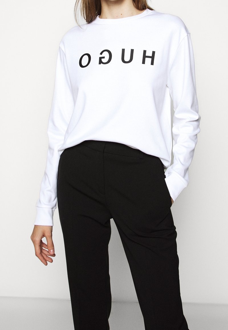 Witte sweatshirt met lange mouwen en zwarte "HUGO" tekst die ondersteboven is gedrukt, gecombineerd met zwarte broek. Eenvoudig, ontspannen ontwerp en pasvorm.