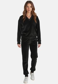 Set di abbigliamento casual nero composto da una maglietta a maniche lunghe con scollatura a V e pantaloni abbinati, texture liscia, polsini aderenti e vestibilità informale.