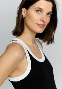 Zwarte tanktop met ribbeltextuur, witte afwerking op de halslijn en armsgaten, en een aansluitend ontwerp dat het schoudergedeelte accentueert.