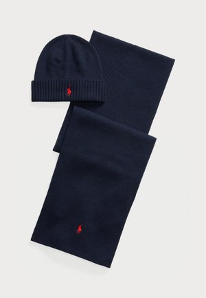 Set composto da berretto a maglia e sciarpa in navy realizzati in tessuto morbido, con texture a coste e piccoli accenti rossi del logo su entrambi i pezzi.
