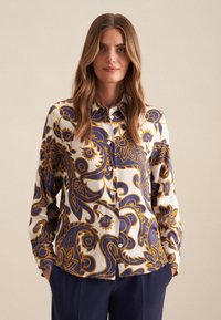 Blusa a maniche lunghe bianca con intricate fantasie paisley blu navy e oro, dotata di chiusura a bottoni e dal fit rilassato.