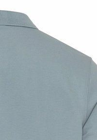 Jasnoniebieska koszulka polo z teksturowanej tkaniny, z prążkowanym kołnierzykiem i skośnym szwem na ramionach, podkreślająca gładki i estetyczny design.