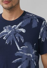 Navyblauwe katoenen t-shirt met een lichtblauw palmbomenprint. Ronde hals met korte mouwen, zachte textuur en casual ontwerp.