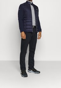 Marinblå vadderad jacka med grå dragkedja, svarta byxor och svarta Nike-skor. Har en ståkrage och en sidologotyp på jackan.