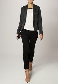 Blazer texturé gris sur un haut blanc, associé à un jean skinny noir et des talons à bride beige, le tout complété par une pochette noire.