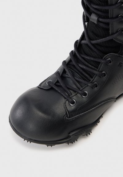 Bottes de combat noires avec un bout arrondi, tige en cuir lisse, lacets, passants, languette en maille, et une semelle robuste et crantée pour l'adhérence.