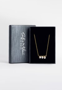 Guldkæde med tre hvide perler, præsenteret i en smykkeboks med sort fløjl indvendigt og et sølvlogo på ydersiden.