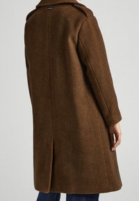 Cappotto in lana a spina di pesce marrone con maniche lunghe, colletto a risvolto e spacchetto posteriore visibile, che mostra una finitura testurizzata.