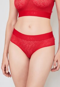 Red lace underwear featuring wavy patterns, a wide solid red waistband with "JOOP! JEANS" embossed, and a soft, stretchy texture.