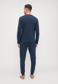 Top navy cu mâneci lungi și pantaloni asortați dintr-un material moale. Cămașa are un decolteu rotund, iar pantalonii dispun de manșete cu nervuri.