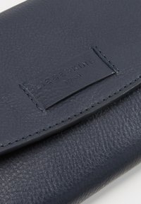 Tmavě modrá kožená peněženka s texturovaným povrchem. Obsahuje obdélníkový štítek značky a viditelné prošívání podél okrajů.