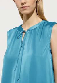 Himmelblause Satinbluse mit Rundhalsausschnitt, kleinen Bindedetails und ärmellosem Design. Glatte Textur und minimalistische Gestaltung.