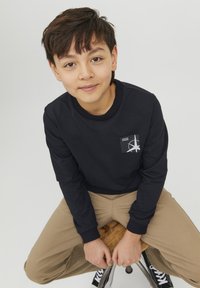 Felpa navy con collo a giro, dotata di un piccolo patch con logo. Abbinata a pantaloni beige chiaro e sneakers nere.