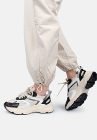 Chunky Sneaker in Creme, Schwarz und metallisch silbernem Mesh. Verfügt über eine strukturierte Sohle, ein schnürbares Design und gepolsterte Knöchelunterstützung.