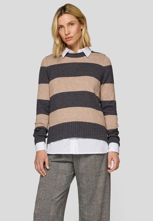 Gestreifter Pullover in Beige und Dunkelgrau, mit geripptem Saum, getragen über einem weißen Hemd mit Kragen. Das Model steht vor einem neutralen Hintergrund.