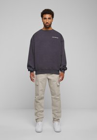 Sudadera gris de gran tamaño con el texto "PROHIBIDO", combinada con pantalones cargo beige con bolsillos y zapatillas blancas. Diseño simple y casual.