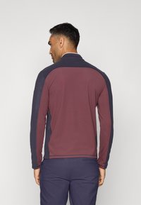 Pullover a maniche lunghe in bordeaux e navy. Tessuto morbido, colletto alto, design con pannello spalla a contrasto e silhouette aderente.