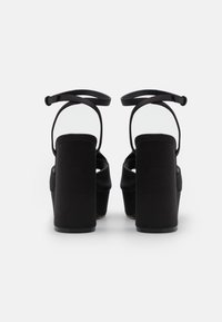 Černé sandály na podpatku s měkkým textilním svrškem, nastavitelným řemínkem kolem kotníku a masivním blokovým podpatkem pro stabilitu. Minimalistický design s otevřenou zadní částí.