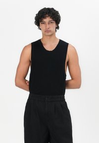 Black sleeveless ribbed tank top with a wide neckline; fitted design. Paired with black, slightly loose-fitting trousers with an elastic waistband.