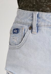Shorts en denim bleu clair avec un ourlet effiloché et des détails usés. Dotés d'une étiquette de marque tissée et d'une fermeture à bouton en métal.