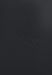 Materiale impermeabile nero con logo in rilievo "RAINS". Texture liscia, design minimalista senza ulteriori motivi o accenti.