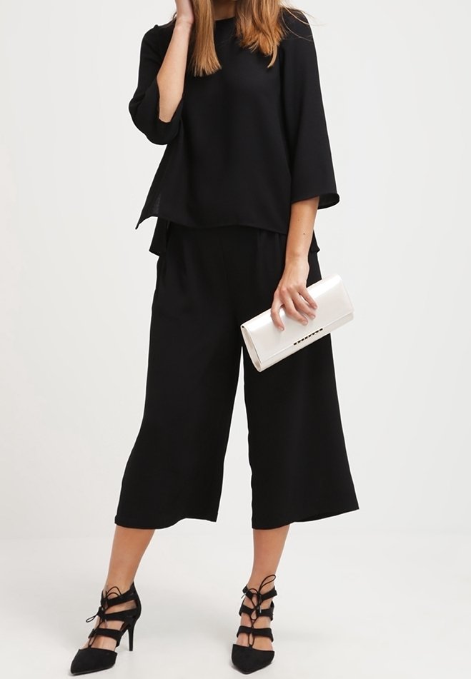Svart, lös passform topp med 3/4 ärmar, matchad med svarta vida byxor. Accessoriserad med en vit clutch och svarta klackskor med remmar.