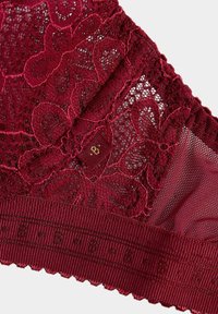 Bordeauxroser Spitzen-BH mit Blumenstickerei, geschwungenen Kanten, strukturiertem Bund und einem goldfarbenen Akzent mit dem Buchstaben "B" auf der Innenseite.