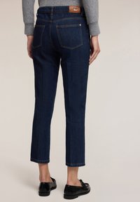 Tmavě modré džíny s rovnými nohavicemi, s zadními kapsami, značenou koženou nášivkou na pase a končící až u kotníků.