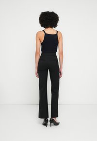 Czarne, eleganckie spodnie o wysokim stanie i smukłej sylwetce, zestawione z dopasowanym granatowym topem na ramiączkach. Gładka tkanina i subtelne tylne kieszenie.