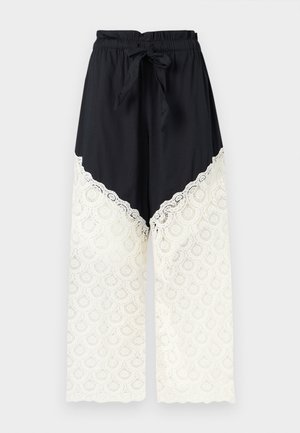 Pantalon noir à jambes larges avec taille élastique et lien, présentant un détail en dentelle blanche du milieu de la cuisse jusqu'à l'ourlet.