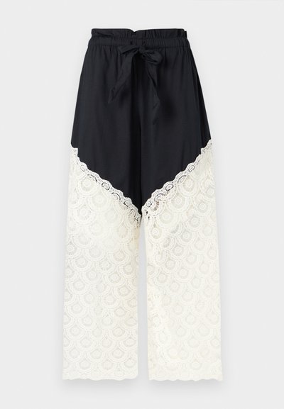Pantalon noir à jambes larges avec taille élastique et lien, présentant un détail en dentelle blanche du milieu de la cuisse jusqu'à l'ourlet.