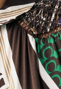 Tela marrón, verde y blanca con patrones geométricos y circulares, que presenta texturas recogidas, arrugadas y de malla.