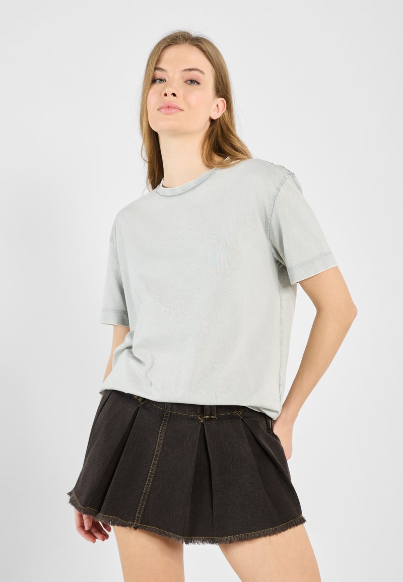 Light gray, cotton T-shirt with a crew neckline and short sleeves, paired with a black denim A-line skirt featuring pleats and frayed hem.
