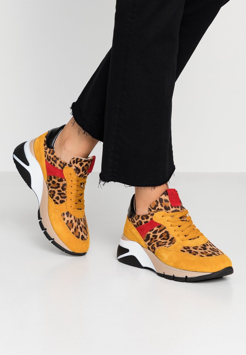 Leopardmönstrade sneakers med gul mocka, svarta accenter, röda detaljer och en upphöjd vit och svart sula, med snörning.